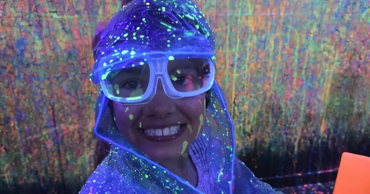 Smiling guest wearing safety goggles in the glow-in-the-dark Splatter Room